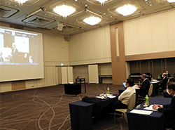 開会挨拶をする貫代表幹事の姿が映し出されたスクリーンを見る広島の参加者